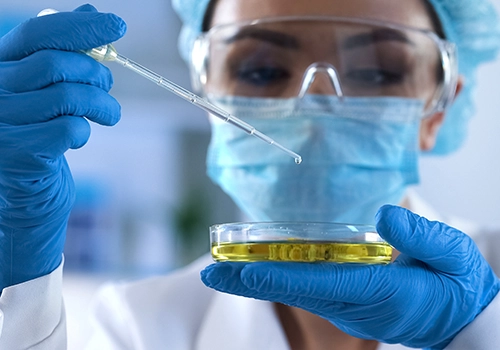 closeup of petri dish and pipette held by scientist in full ppe gear.