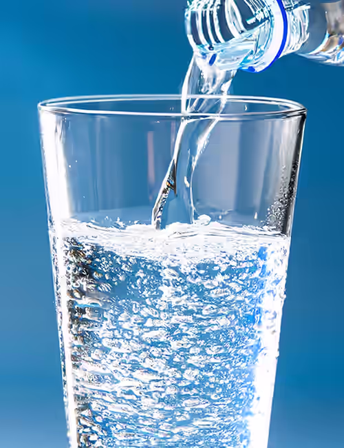 Water glass being filled by bottle on blue background. Paceº Water management and drinking water testing services for the Hospitality Industry.