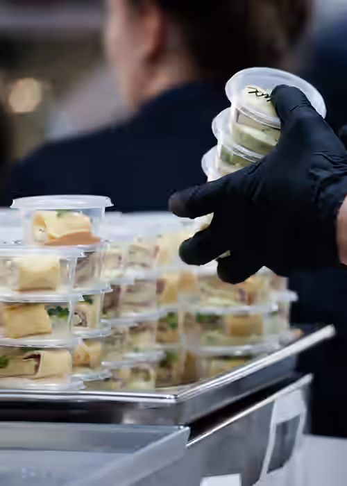 Shelf Life Studies. Caterer holding containers of food with gloved hands.